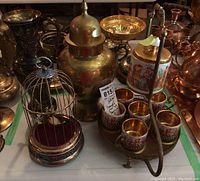 Photo showing the full tea service set, bird cage, vase, and temple jar together, highlighting the tea set with a tag, the bird cage with the bird inside, and metallic decorative items in the background.