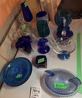 Photo showing assortment of blue glass and crystal decorative items including bowls, small vases, and keepsake boxes with price tags attached.