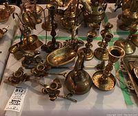 Photo shows the full assortment of brass items including multiple candlestick holders, crumb catcher, soap dish, teapot figurine, arranged on a surface