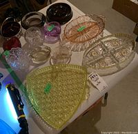 Overview of colored glass items spread on white table including platters, divided dishes, bowls, ashtray, and art glass pieces
