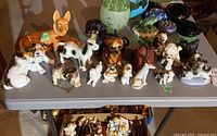 Photo of 21 assorted ceramic and porcelain dog figurines in various colors and sizes on a gray table