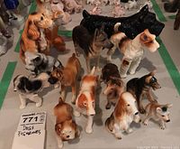 Group photo showing ceramic dog figurines of various breeds, different colors, and sizes between 3-7 inches, placed on a white surface.