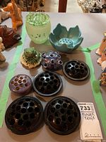 Nine assorted flower frogs on display showing variety in colors, materials, and designs across the lot