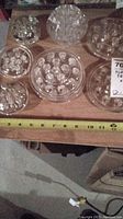 Top-down photo showing eight clear glass flower frogs on a wooden surface with measuring tape indicating size about 4 inches.