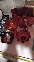 Overview of ruby red glass stemware and bowls including footed bowl, vase, stemware, and decorative bowls grouped together on a table.