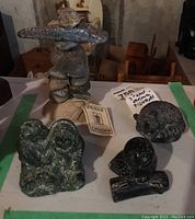 Photo showing the Inuksuk stone sculpture, the Inuit children carving, and three small animal carvings (wolf, owl, raccoon) on a flat surface.