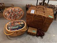 Lot contents including large wicker picnic basket, oval sewing basket with floral lining and plastic stir sticks, small rectangular wicker basket, and heart-shaped fabric souvenir from 1944.