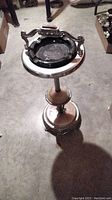 Full view of the vintage ashtray stand showing white marble top, glass ashtray, metal handles, and ornate metal pedestal base.