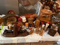 Overview photo showing vintage mantel clock, salt and pepper shakers, wooden bowls, bookends and wooden boxes arranged on a table.