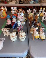 Photo showing several porcelain and ceramic salt and pepper shakers arranged on a gray table, including cats, cows, owls, and human-like figures with colorful detailing.