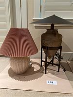 Two different table lamps displayed side by side on floor with measurements noted. Lamps have different styles, one ceramic with pink pleated fabric shade, the other rustic pottery with black metal stand and dark metal shade.