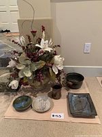 Photo showing entire artificial flower arrangement in decorative pottery vase with ceramic and pottery pieces arranged in front.
