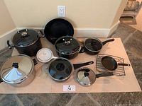 Overview of the full set of pots and pans with lids and accessories on paper covering on floor.