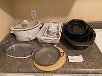 Cookware lot including Rival Crock-Pot, baking pans, cast iron pan, ceramic plate, and glass dish.