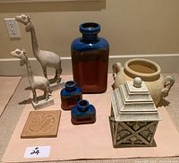 Group photo showing all decorative items: two giraffe sculptures, three blue-brown glazed vases, beige urn, decorative box, and tile.