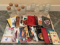 Full view of 8 glass containers and 17 assorted cookbooks laid out on floor