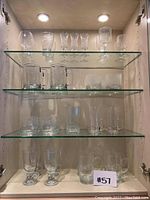 Full view of glassware set on glass shelves showing various types of drinking glasses and mugs.