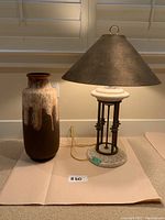 Floor vase and lamp set shown side by side on paper with natural light from window blinds.