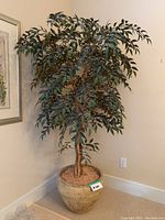 Large artificial tree in decorative beige ceramic pot against a wall corner.