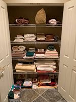 Wide view of wire shelving holding neatly folded linens including towels, blankets, and small fabric items at bottom shelf.