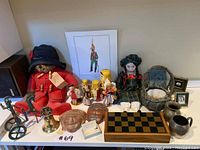 Overview of all items: Paddington Bear, doll, nested dolls, masks, chessboard, metal sculpture, frames, bell