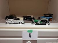 All five diecast model cars arranged in a row on white shelf, showing overall lot