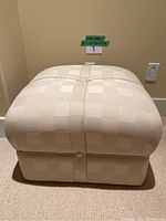 Front view of beige checkered fabric ottoman with button and strap detail