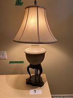 Pair of table lamps with beige bell-shaped fabric shades and urn-shaped textured bases on decorative dark curved stands.