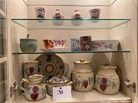 Shelf display with an assortment of pottery items including jars, cups, plates, and a small flowerpot, all with colorful hand-painted designs.