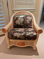 Front view of rattan chair with floral patterned cushions and visible wood engraved details on the arms and lower front panel.