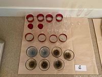 Full lot of glassware arranged on floor, showing red-rimmed glasses, clear stemmed glasses, red lids, and dessert dishes.