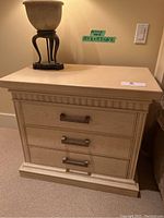 Front view of one bedside table showing three drawers and top surface with a decorative item on top.