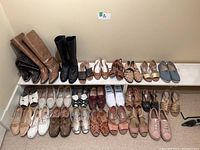 Overview of 26 pairs of women's shoes arranged in rows including boots, sandals, flats, and runners in various colors and styles.