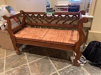 Front view of the wood bench with curved armrests and banana leaf patterned seat cushions.