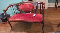 Front view of antique wooden settee with red velvet-like upholstery and carved wood frame.