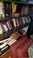 Full view of three black shelves filled with assorted books, various sizes and titles, with a red suitcase or cushion visible on floor near bottom shelf