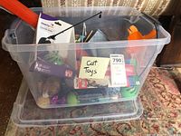 Photo of clear plastic tote filled with various colorful cat toys, some loose inside, with label 'Cat Toys' on the tote.
