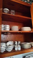 Cabinet shelves showing stacked china including cups, saucers, and plates.