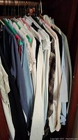 Men's and women's shirts and blouses hanging in a closet, showing variety of colors and styles.