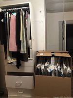 Photo showing ladies skirts and shirts hanging on white dresser next to a box containing men’s neckties individually packaged in plastic.