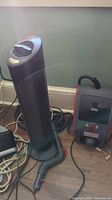 Photo showing both the Haan floor sanitizer (box-shaped, black and red) and the Sharper Image Ionic Breeze (tower-shaped air purifier) side by side on wooden floor.