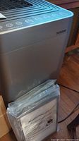 Overall perspective of air purifier with sealed user manual displayed in front.