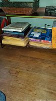 Photo showing stacked office supplies including spiral notebooks, packs of paper and boxes likely with shipping or packing labels, on wooden surface.