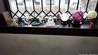 Wide image showing the window ledge displaying multiple paperweights, figurines, and glass balls including colorful spheres, carved white piece, and animal figurines.