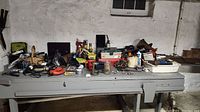Wide view of workbench covered in assorted tools and supplies including paint cans, power tools, hardware items.