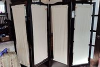 Full view of the room divider showing four hinged dark brown wooden panels with beige canvas inserts.