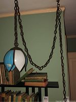 Full view of the lotus style swag lamp hanging from the ceiling with heavy metal chain above a bookshelf featuring old books.