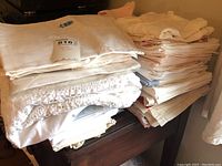 Stack of white table linens and napkins with lace detail on wooden furniture