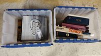 Two totes side-by-side, one containing vinyl records and one containing board games with visible game titles Sorry and Trivial Pursuit
