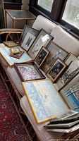 Overview of framed artworks arranged on couch, showing multiple pieces with various subjects and frame styles.